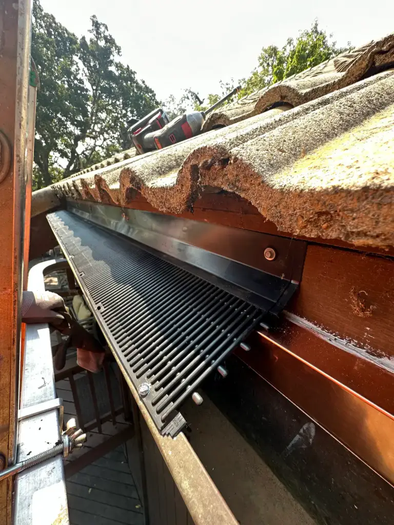 Brown gutter with a black guard tucked under a tile roof edge