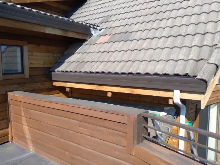 Brown gutter and downspout on a tile-roofed house with wood siding and a deck