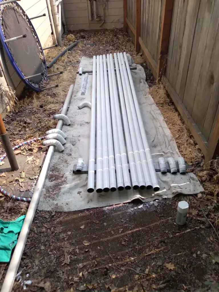 Lengths of gray downspout laid out on a tarp in a side yard