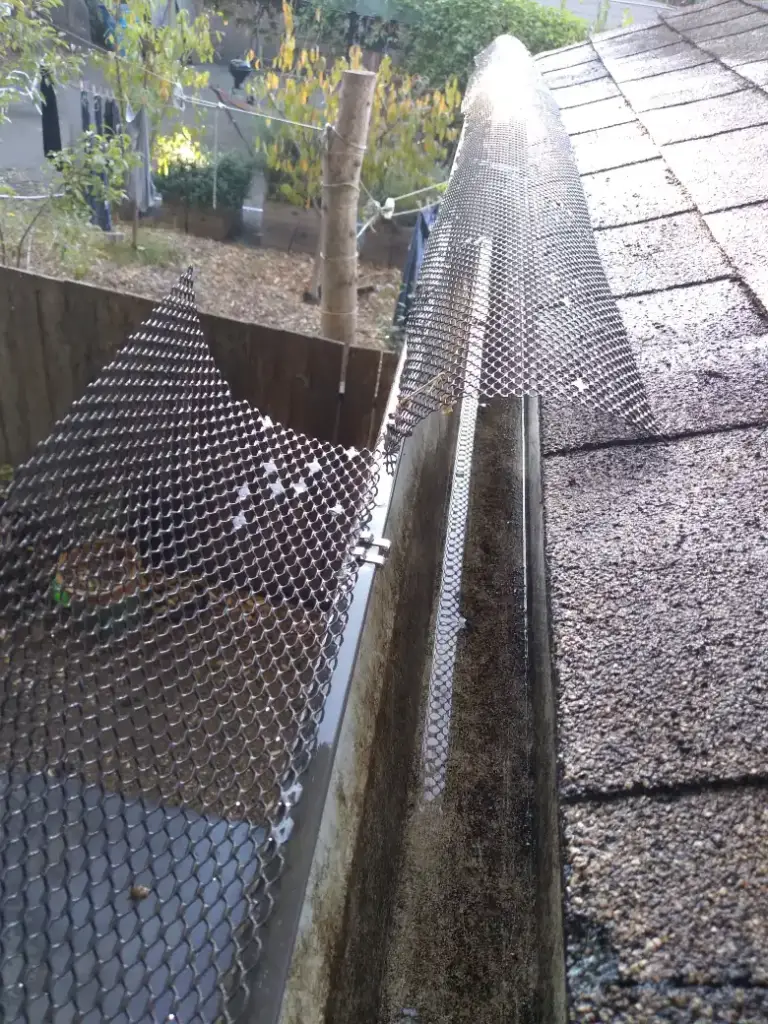 Expanded metal gutter guard being fitted over a gutter along shingles