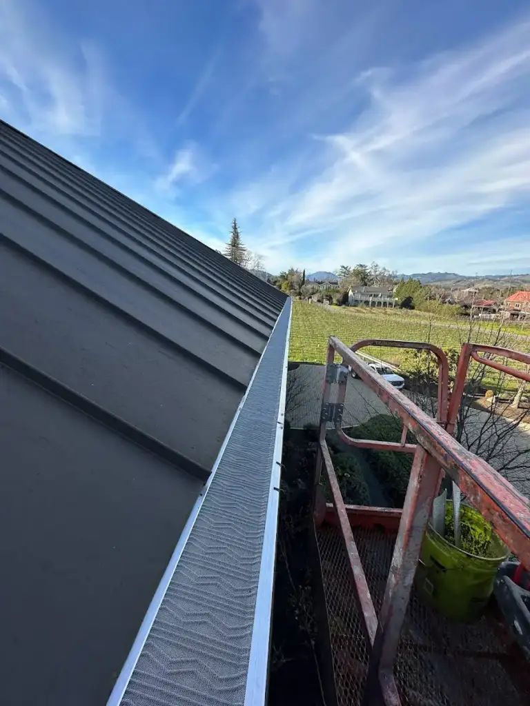 Gutter guard along the edge of a dark metal roof above a backyard