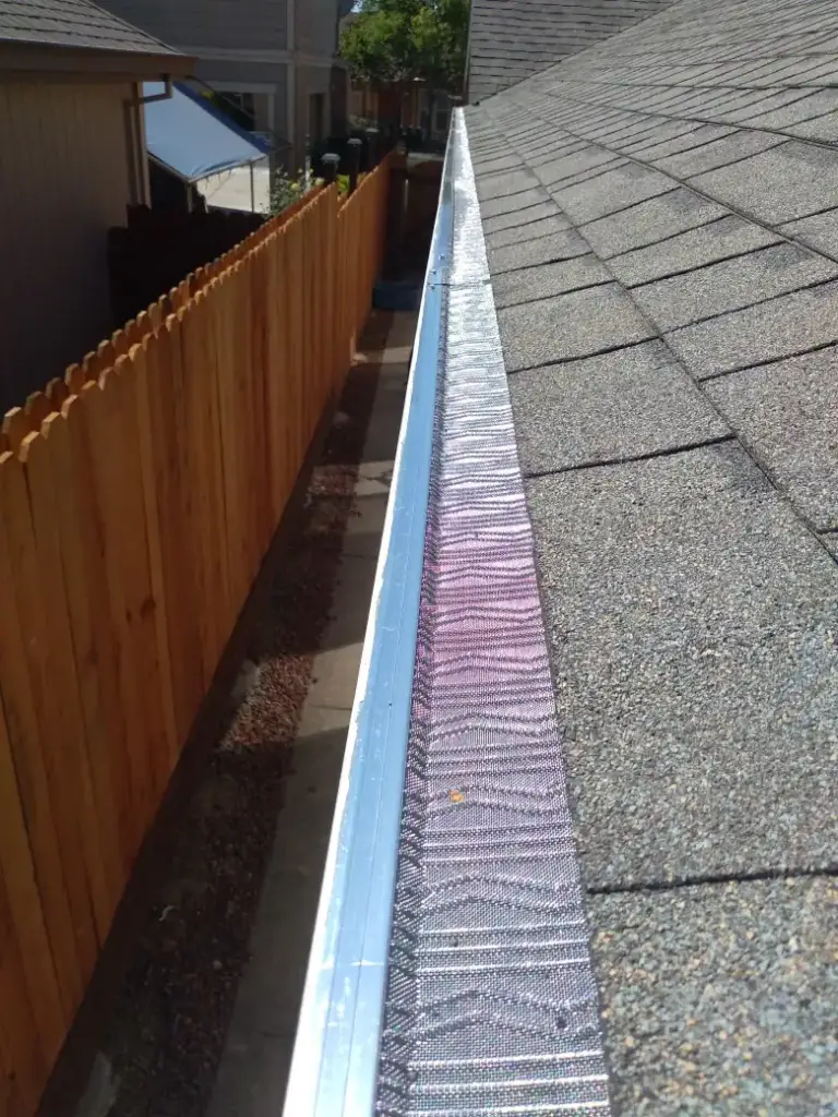 Mesh gutter guard running the length of a gutter above a wood fence