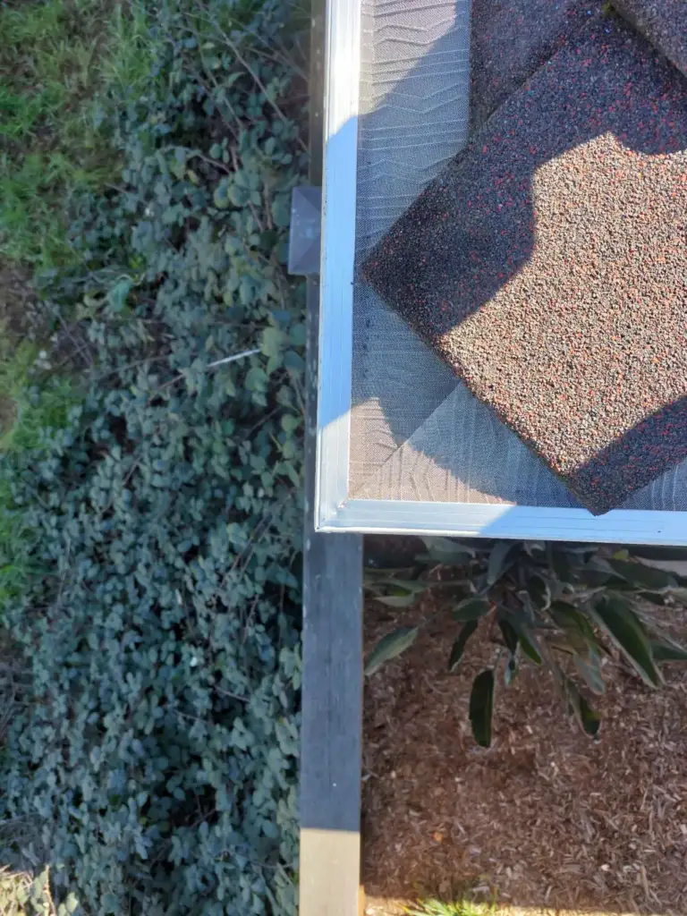 Close-up of a mesh gutter guard at a roof corner with ivy below