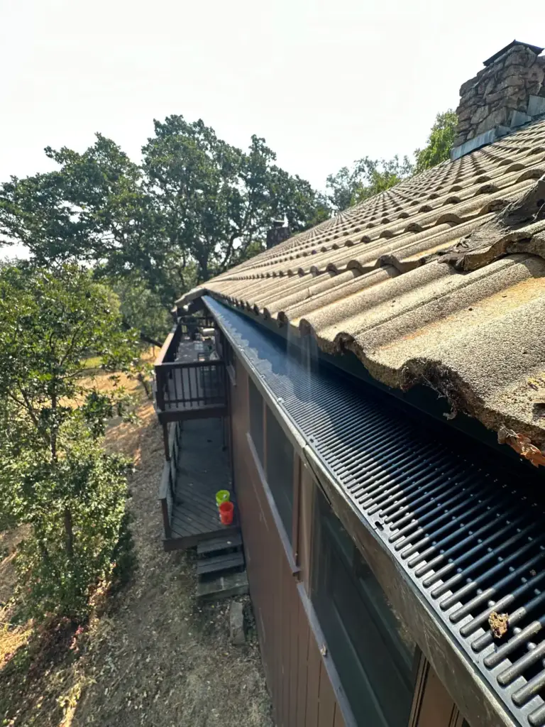 Black gutter guard installed under the edge of a clay tile roof above a wooden balcony