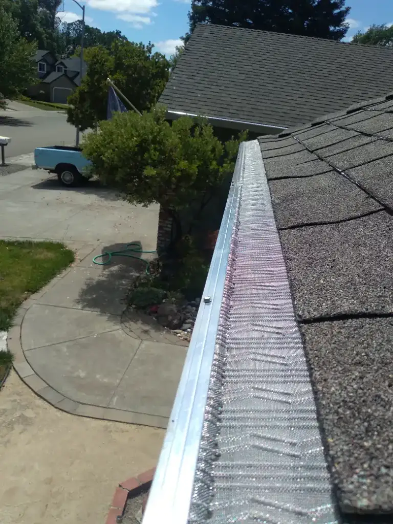 Micro-mesh gutter guard along a shingle roof edge above a driveway
