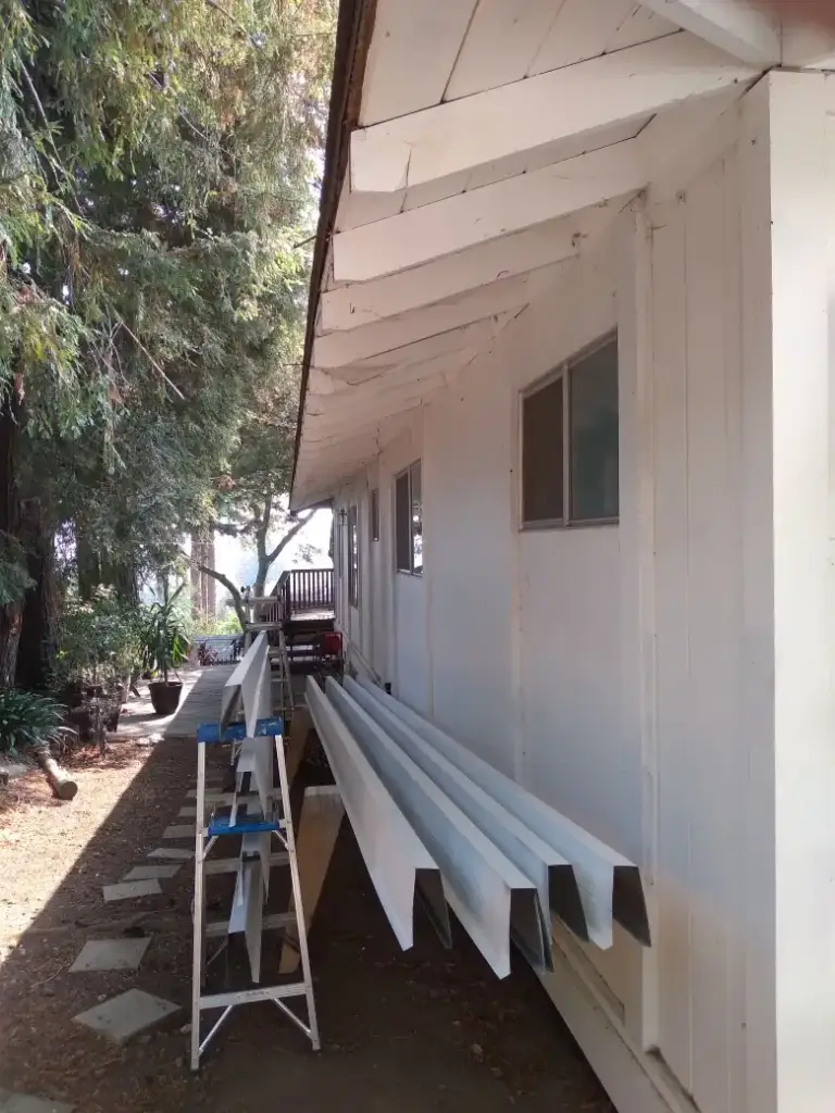 Lengths of new white gutter laid along the side of a house before installation
