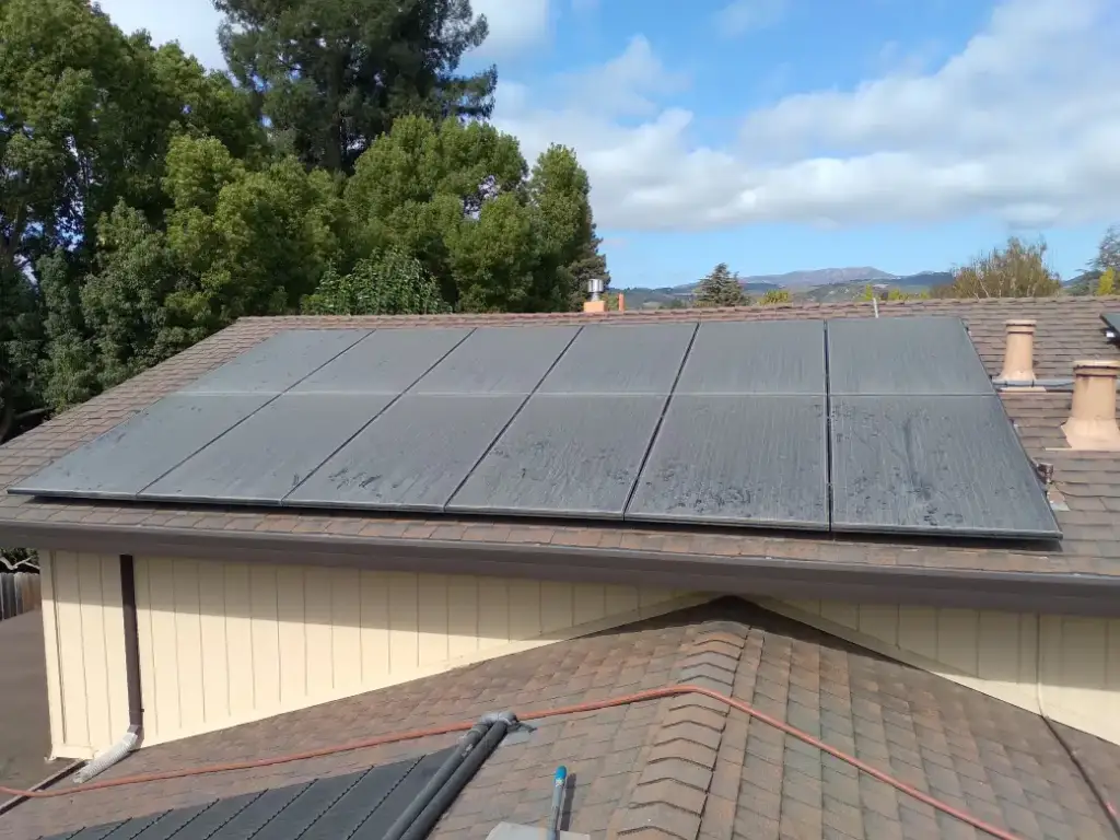 Solar panels on a roof above a lower tile roof, with hills in the distance