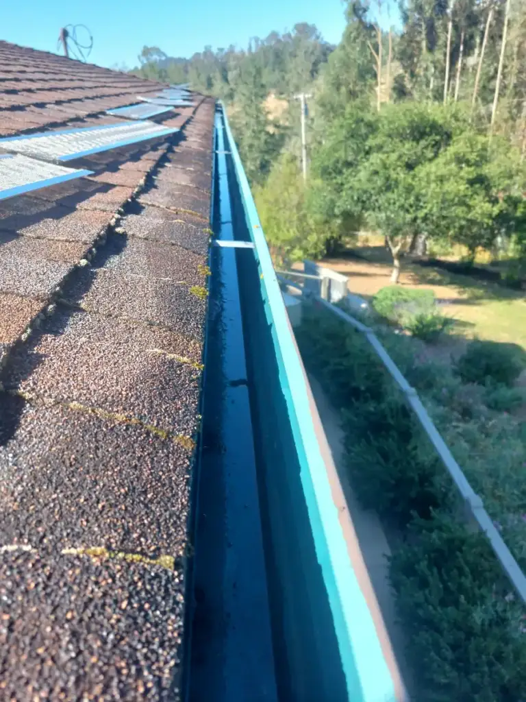 Teal gutter cleared of debris along a shingle roof above a hillside yard